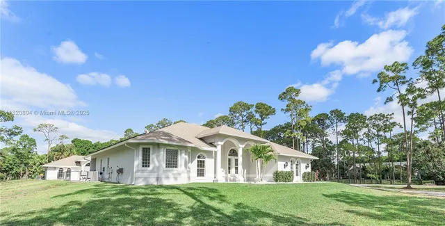 a view of a white house with a big yard and large trees