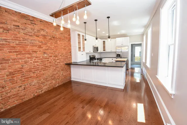 a large kitchen with stainless steel appliances a large counter top a wooden floor and a window