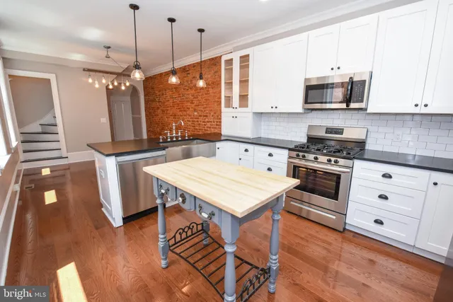 a kitchen with stainless steel appliances a stove a sink a microwave a refrigerator and white cabinets