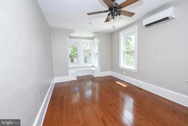 an empty room with wooden floor windows and fan