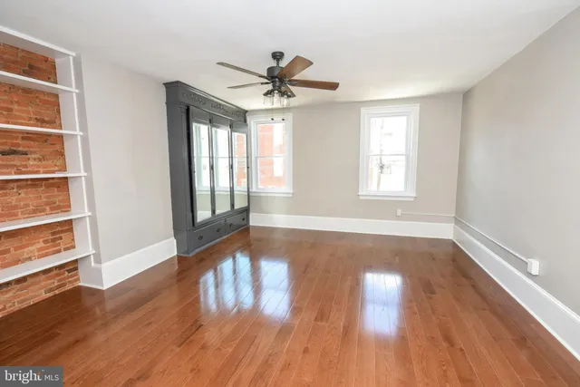 an empty room with wooden floor chandelier fan and windows