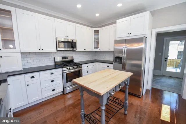 a kitchen with stainless steel appliances granite countertop a refrigerator a sink dishwasher a stove and white cabinets with wooden floor