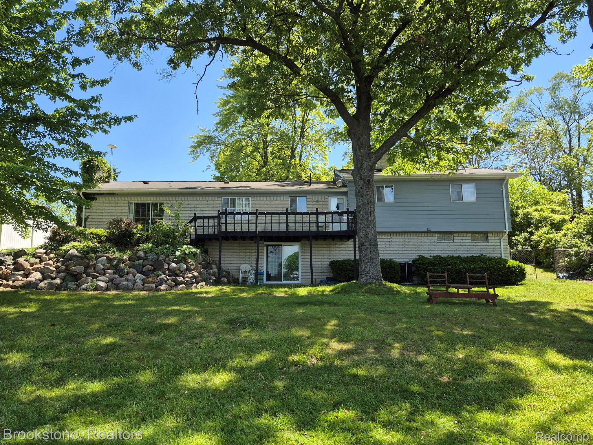 4295 Sashabaw Road Waterford, MI 48329 - Photo 2 of 37 Expansive rear yard featuring a large deck, lower-level patio access, and a rock retaining wall with established landscaping