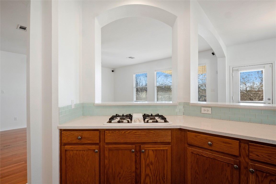 601 Red Hawk Drive Leander, TX 78641 - Photo 11 of 40 Kitchen with brown cabinetry, tasteful backsplash, white gas stovetop, light stone countertops, and wood finished floors