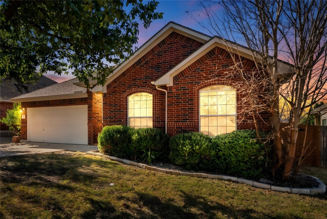 601 Red Hawk Drive Leander, TX 78641 - Photo 36 of 40 Ranch-style home at dusk featuring driveway, an attached garage, a shingled roof, and brick siding