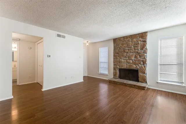 an empty room with wooden floor fireplace and windows