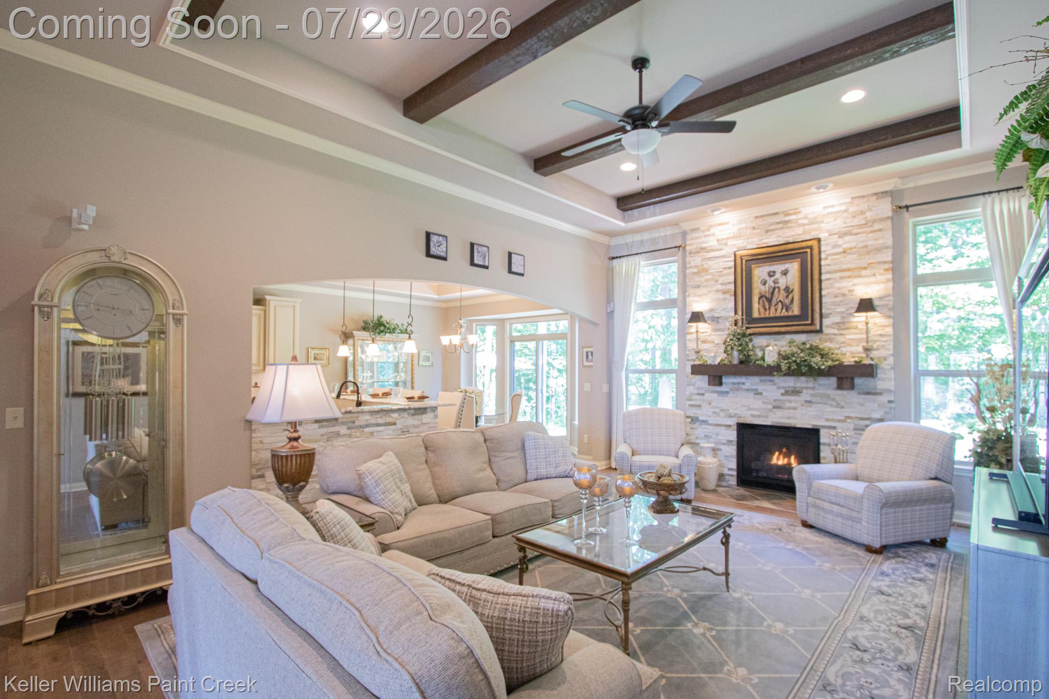 Living area featuring a stacked stone fireplace with a wood mantel, exposed ceiling beams, recessed lighting, and an arched doorway to an additional room