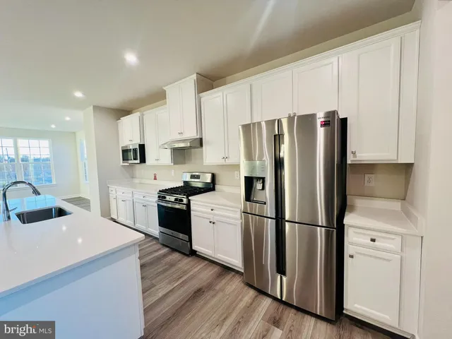 a kitchen with granite countertop a refrigerator stove and white cabinets