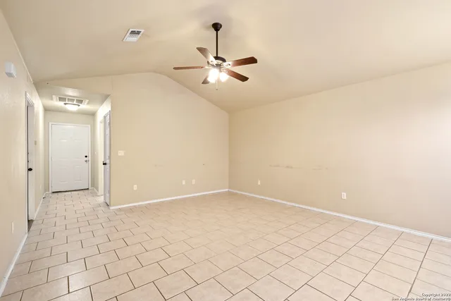 an empty room with kitchen view and a chandelier fan