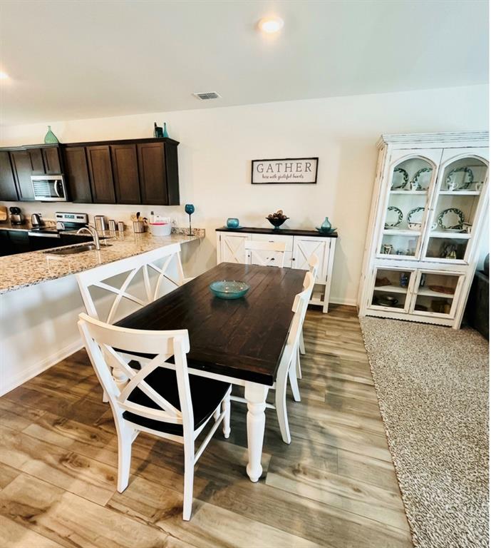 196 Cattlemans Crk Road West Newark, TX 76071 - Photo 6 of 31 Open-concept dining area featuring wood-finish flooring, a kitchen island with stone-look countertops, dark wood cabinetry, and stainless steel appliances