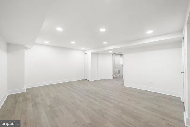 a view of an empty room with wooden floor and a kitchen