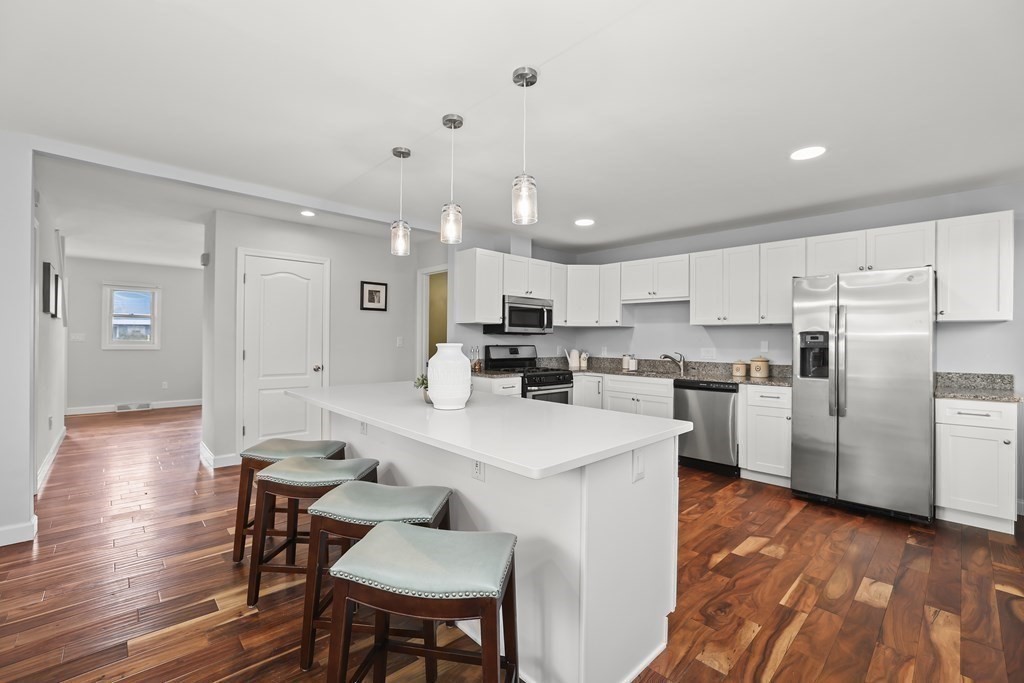 a kitchen with stainless steel appliances granite countertop a refrigerator a sink dishwasher a stove and white cabinets with wooden floor