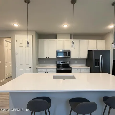 a kitchen with stainless steel appliances a refrigerator a sink a stove a microwave and white cabinets