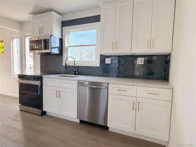 a kitchen with granite countertop white cabinets stainless steel appliances a sink and a window