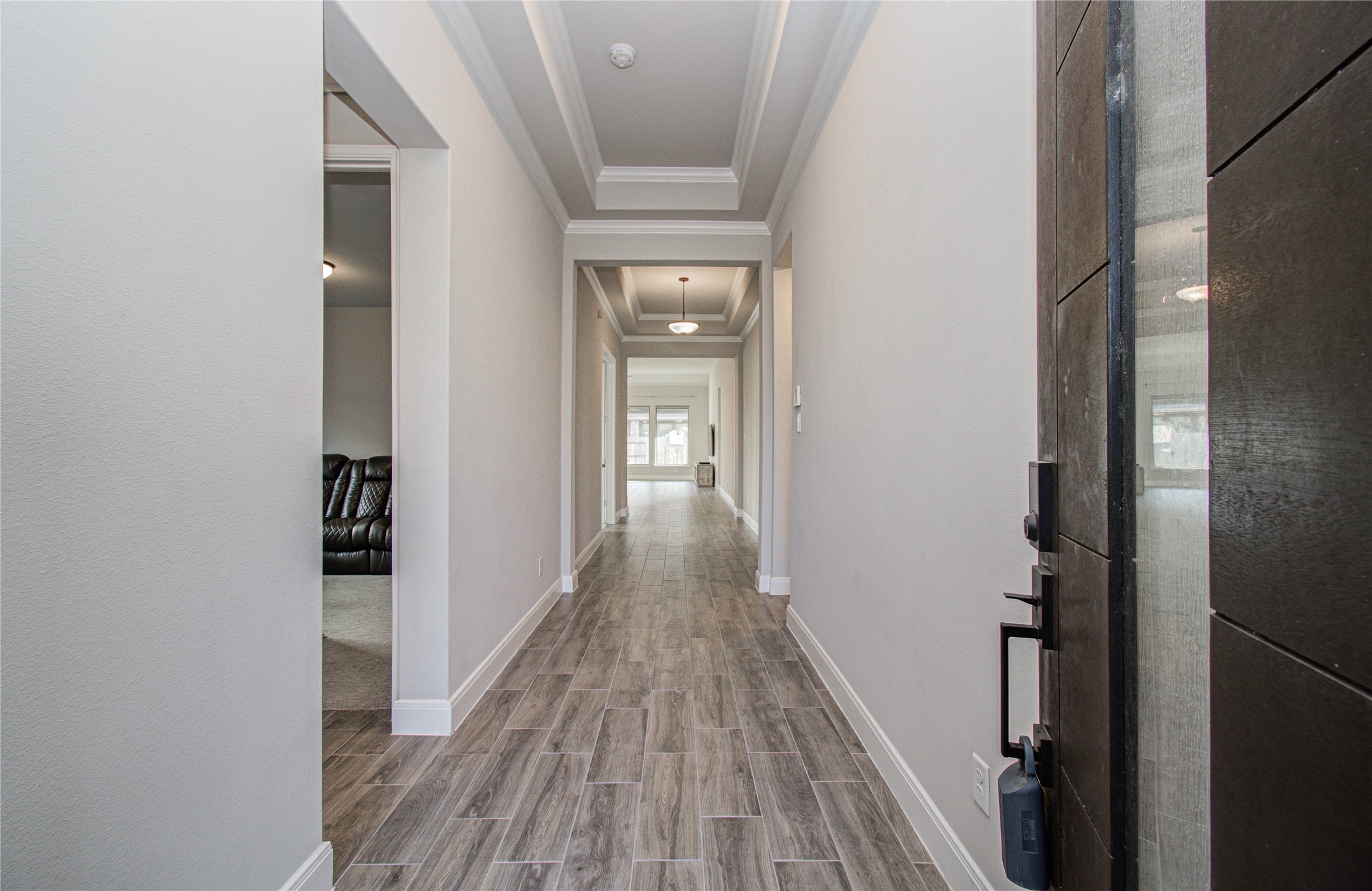 17344 Grand Canyon Road Conroe, TX 77302 - Photo 3 of 49 This photo shows a modern entryway with wood-look tile flooring and neutral-colored walls. It features a coffered ceiling with recessed lighting, leading to a bright, open living space.