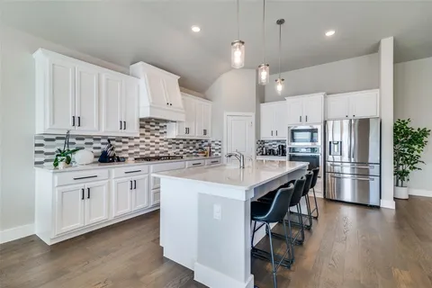 a kitchen with stainless steel appliances kitchen island granite countertop a refrigerator a sink dishwasher a stove and white cabinets with wooden floor