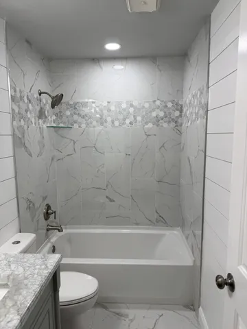 a bathroom with a granite countertop bathtub shower sink vanity and toilet