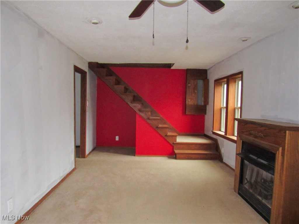 2218 Lake Road Akron, OH 44312 - Photo 3 of 20 Unfurnished living room with stairway, carpet flooring, a glass covered fireplace, and a ceiling fan