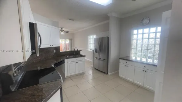 a kitchen with granite countertop a refrigerator a sink a stove and white cabinets