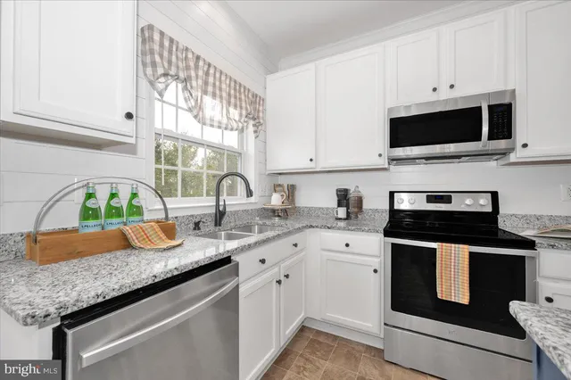 a kitchen with granite countertop stainless steel appliances white cabinets granite counter tops and a wooden floors