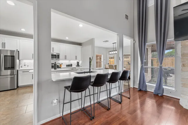 a kitchen with stainless steel appliances kitchen island granite countertop a refrigerator a stove a sink and white cabinets with wooden floor