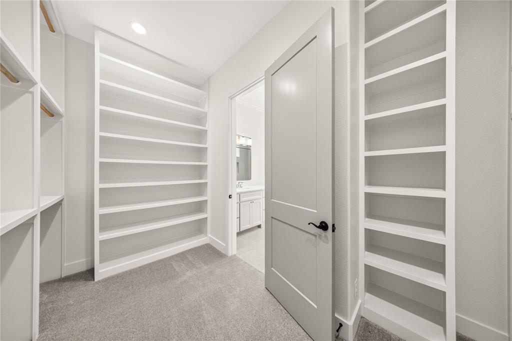 114 Red Bud Road Boyd, TX 76023 - Photo 20 of 32 Spacious walk-in closet featuring extensive built-in shelving, plush grey carpeting, and a light grey paneled door with black hardware