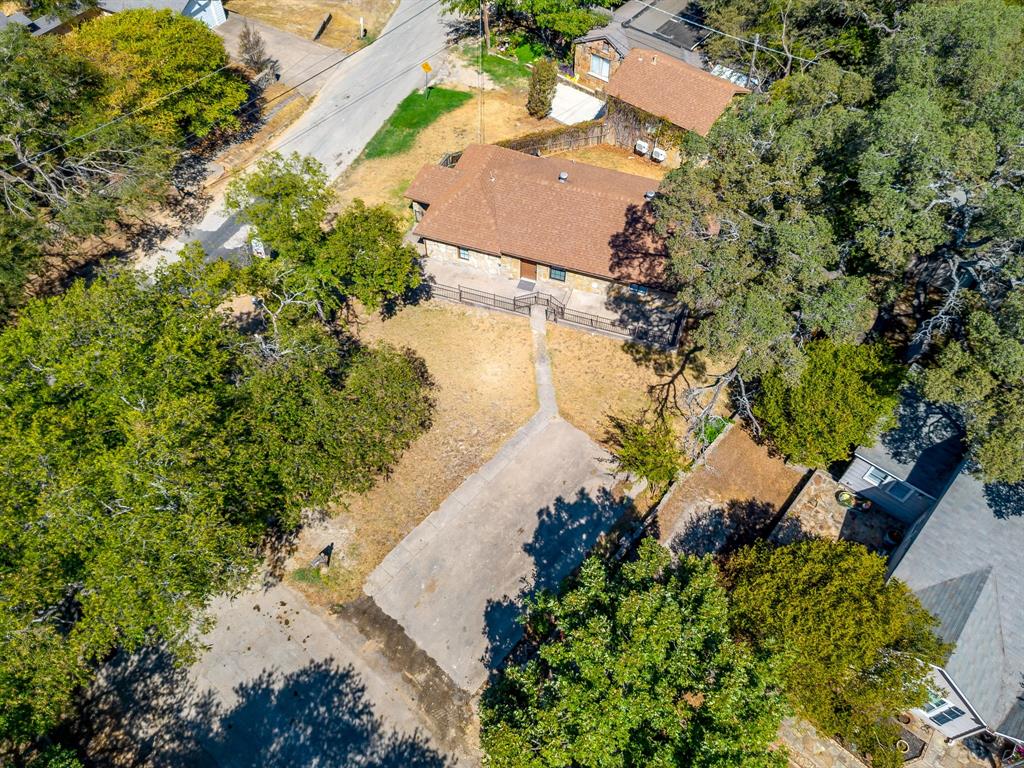 6940 Hatch Road Fort Worth, TX 76135 - Photo 8 of 40 Stone exterior with a brown shingle roof, surrounded by mature trees, featuring a concrete walkway and a paved parking area
