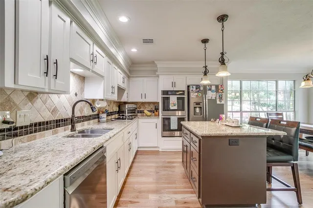 a kitchen with stainless steel appliances granite countertop a stove a refrigerator a kitchen island a dining table and chairs with wooden floor