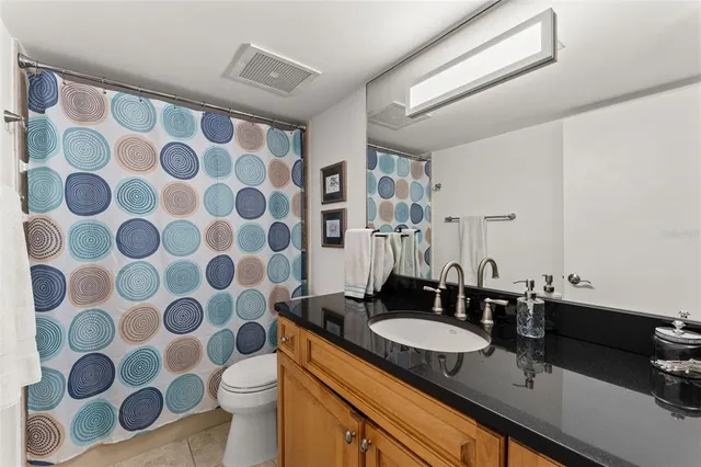 a bathroom with a granite countertop sink a toilet a mirror and shower curtain