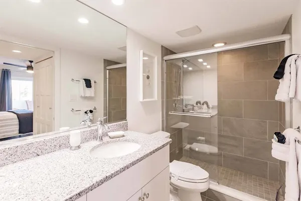 a bathroom with a granite countertop sink a toilet a mirror and shower