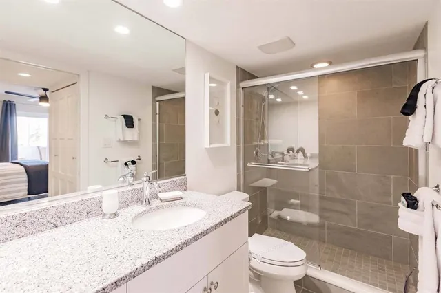 a bathroom with a granite countertop sink a toilet a mirror and shower