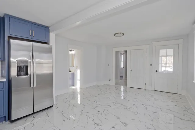 a view of a refrigerator in kitchen and an empty room