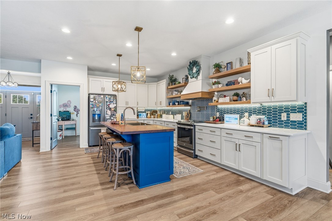 421 Pontius Road Mogadore, OH 44260 - Photo 5 of 50 Gourmet kitchen featuring a central island with seating, wood-finish flooring, white cabinetry, a teal tile backsplash, and stainless steel appliances