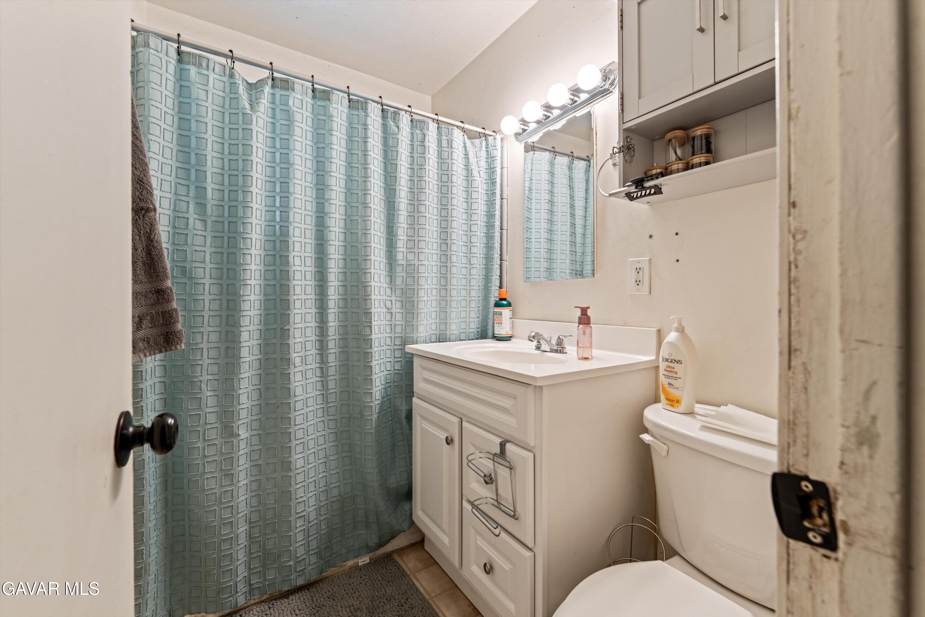 817 Oakwood Street Tehachapi, CA 93561 - Photo 7 of 12 a bathroom with a sink a toilet a mirror and shower curtain