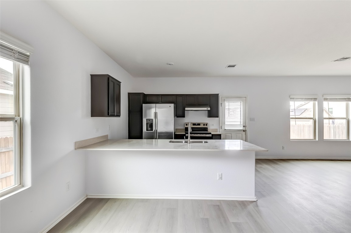 772 Circle Way Jarrell, TX 76537 - Photo 10 of 35 Kitchen featuring appliances with stainless steel finishes, a peninsula, light wood-type flooring, light stone countertops, and dark brown cabinetry