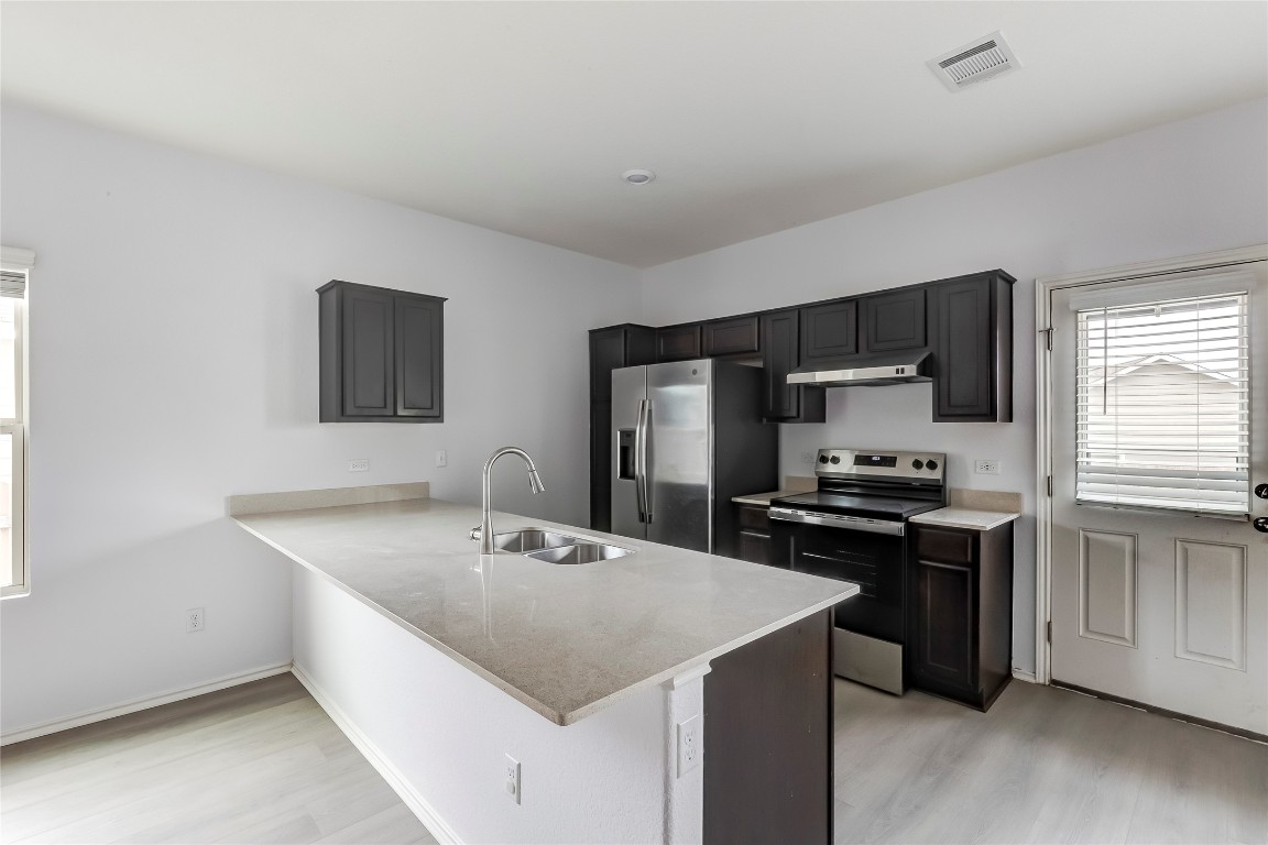 772 Circle Way Jarrell, TX 76537 - Photo 11 of 35 Kitchen with stainless steel appliances, a peninsula, light stone counters, under cabinet range hood, and light wood finished floors
