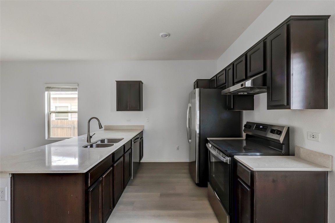 772 Circle Way Jarrell, TX 76537 - Photo 12 of 35 Kitchen with stainless steel appliances, dark brown cabinets, under cabinet range hood, light wood-style flooring, and light stone counters