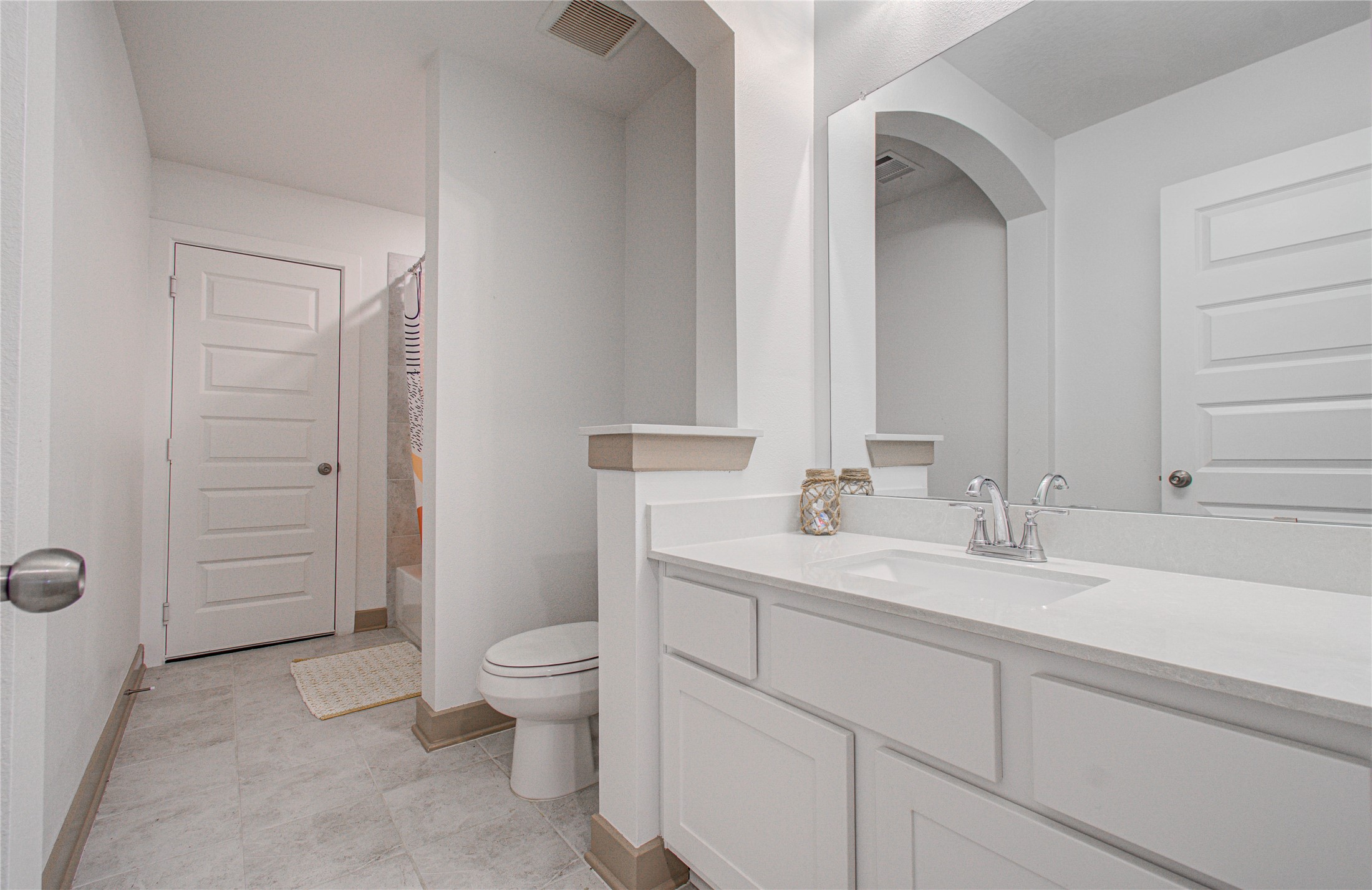 4211 Limestone Terrace Manvel, TX 77578 - Photo 26 of 33 A modern bathroom featuring a spacious white vanity with a large mirror, sleek fixtures, and a neutral color palette. The room includes a toilet and a shower area with a colorful curtain, offering a bright and clean atmosphere.