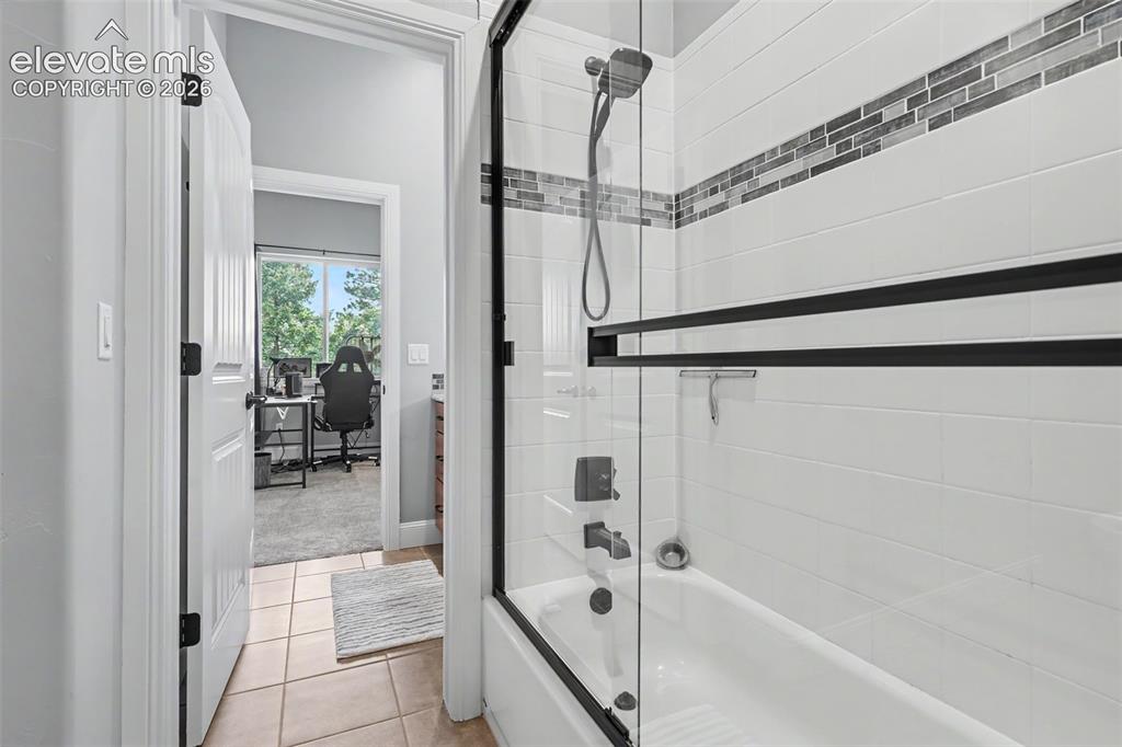 21 Leaming Road Colorado Springs, CO 80906 - Photo 44 of 48 Bathtub with a glass shower enclosure featuring matte black hardware, white subway tile surround, and a decorative mosaic tile accent band