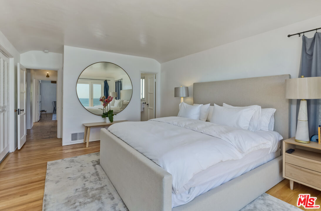 23350 Malibu Colony Road, Unit 109 Malibu, CA 90265 - Photo 22 of 61 a spacious bedroom with a bed a mirror and a table with wooden floor