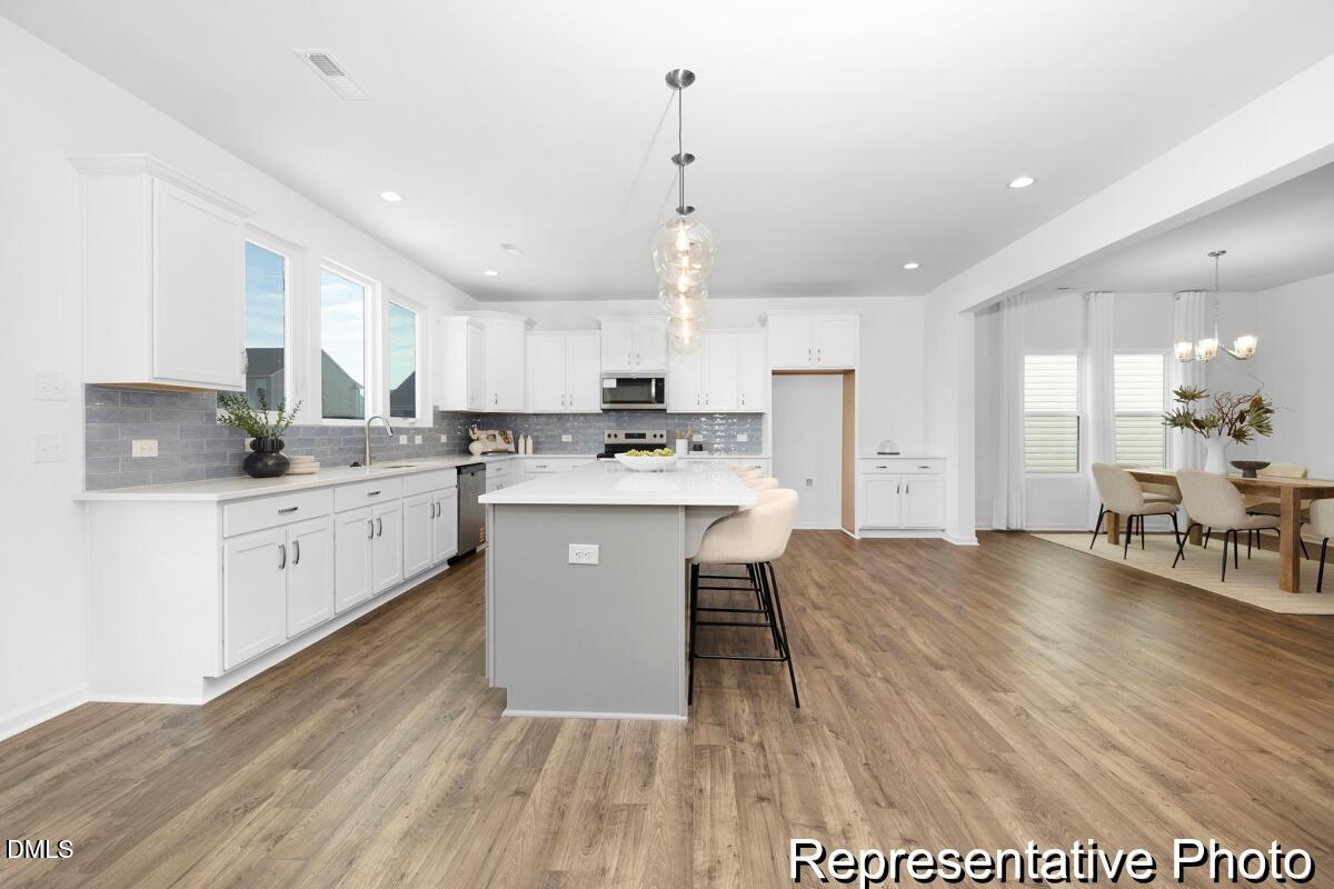 47 Flicker Lane, Unit 188P Angier, NC 27501 - Photo 4 of 38 a kitchen with stainless steel appliances kitchen island granite countertop a stove a sink a refrigerator and white cabinets with wooden floor