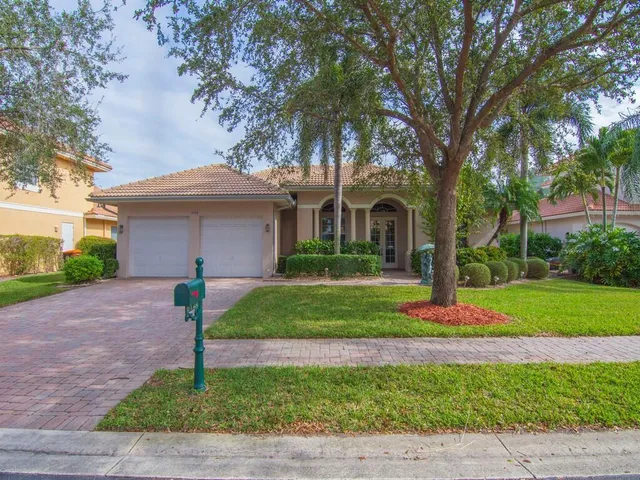 a house that is sitting in the grass with large trees and plants