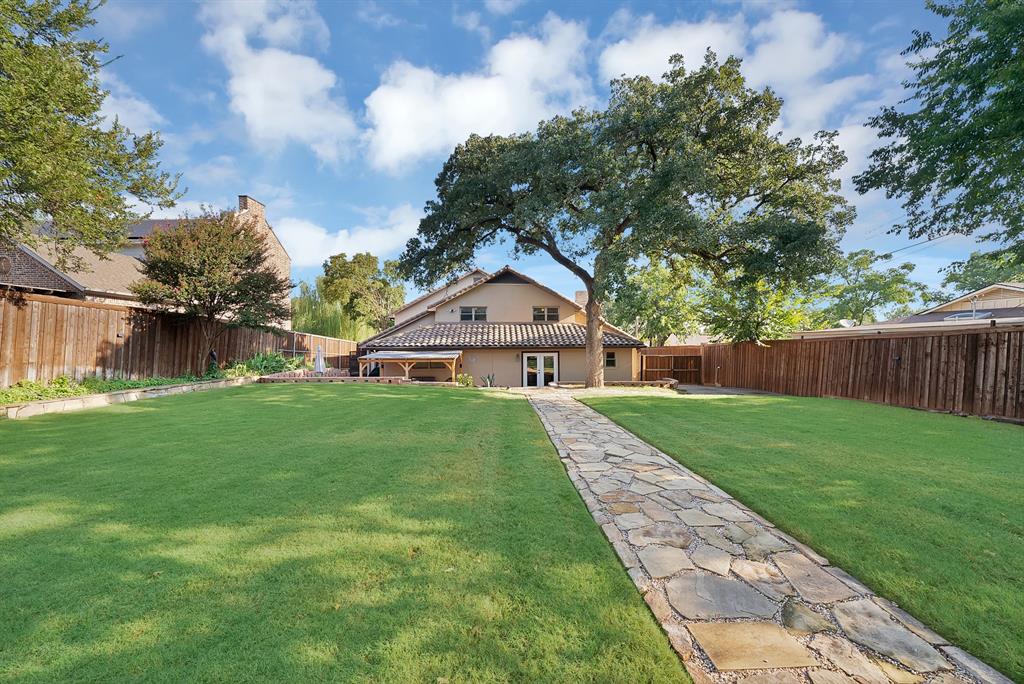 306 Rochelle Boulevard Irving, TX 75062 - Photo 37 of 40 Expansive backyard with a stone-paved walkway, stucco exterior, Spanish tile roof, large mature tree, and covered outdoor structure