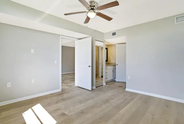 an empty room with wooden floor fan and windows