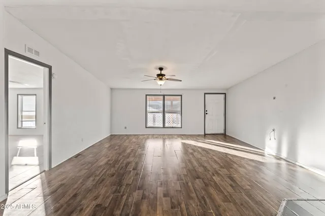 an empty room with wooden floor chandelier fan and windows