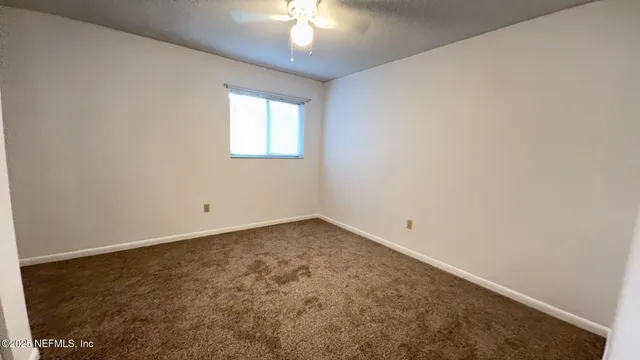 an empty room with a chandelier fan and windows