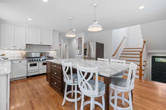 a kitchen with stainless steel appliances a stove a sink a kitchen island with wooden floor and chairs