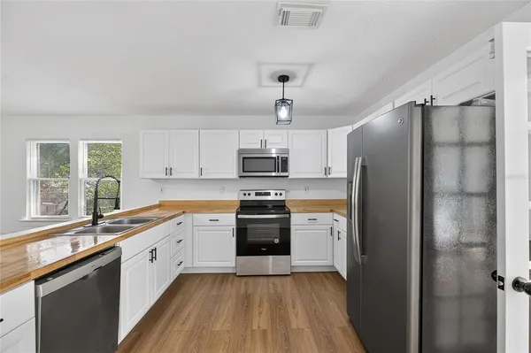 a kitchen with stainless steel appliances granite countertop a refrigerator a sink dishwasher a stove and white countertops with wooden floor