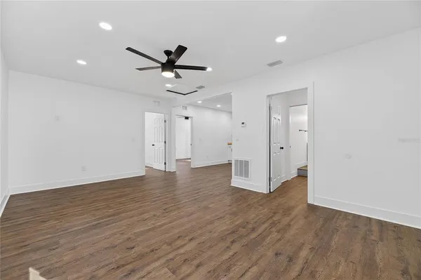 an empty room with wooden floor a ceiling fan and kitchen view