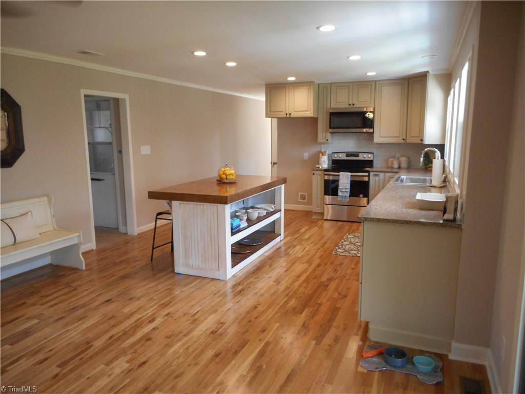 6346 Company Mill Road Climax, NC 27233 - Photo 19 of 30 In this view we are in the den looking into the kitchen. Here we can see that there is some storage space in the kitchen island. We have the engineered wood flooring and the recessed lighting. The open door way just to the left of the kitchen island is to the garage entry door, the laundry room and the half bath. Around the corner and to the left of the stove is the pantry, office room and the side entry door.